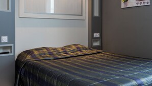 Une chambre à coucher avec un lit, une lampe fixée au mur et une petite étagère.