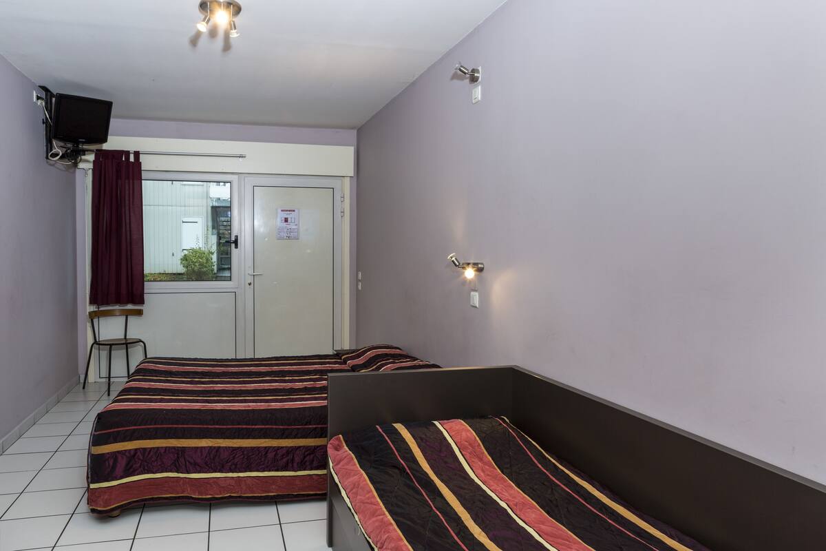A room with two beds, a chair, a TV, and a door with a window.