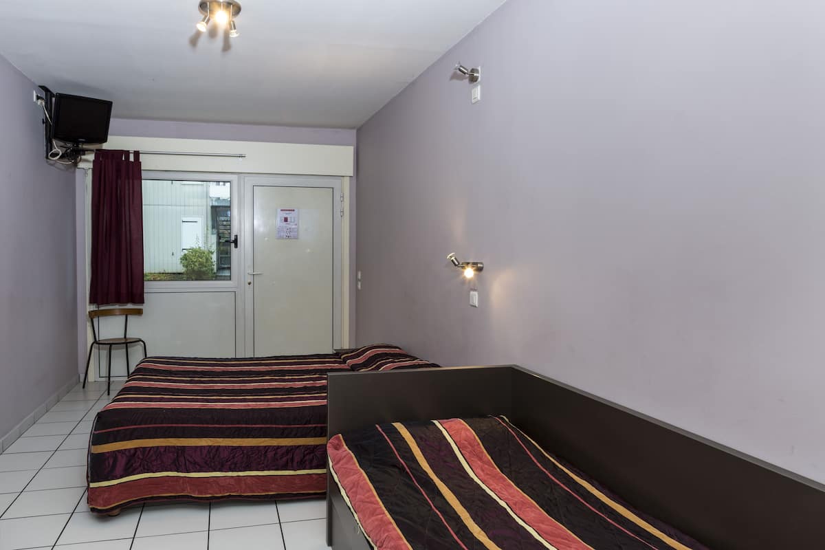 Una habitación con dos camas, una silla, un televisor y una puerta con ventanal.