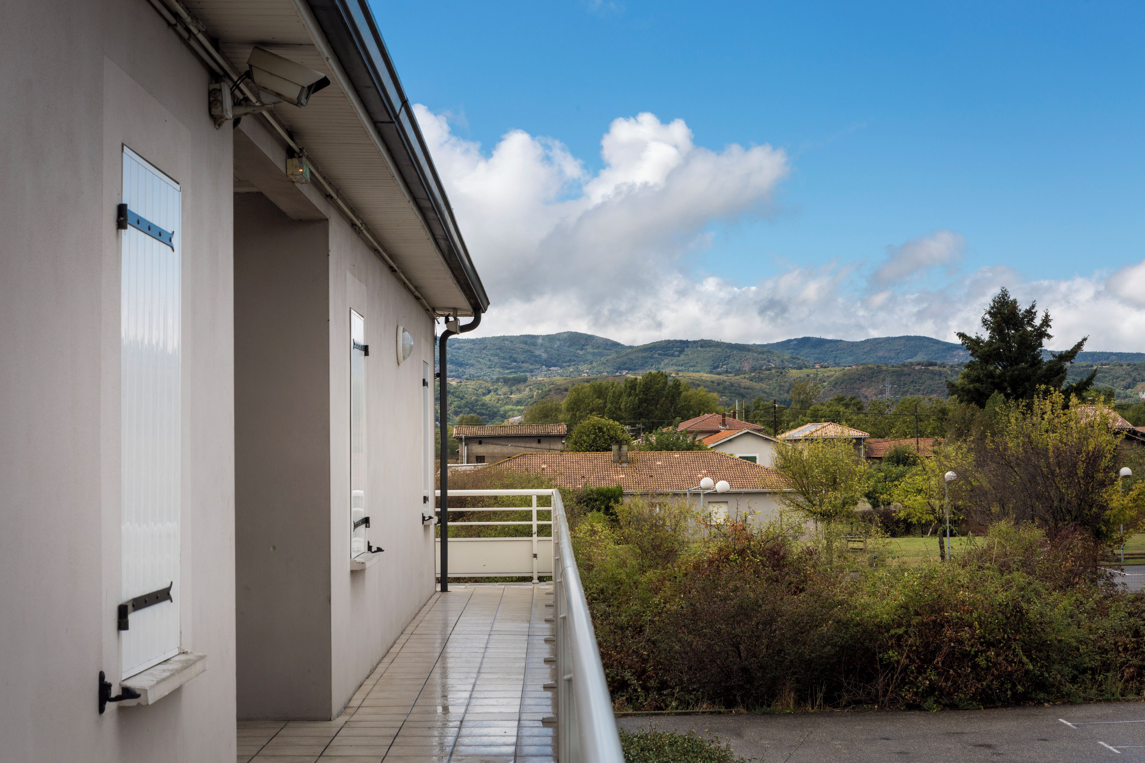 A building with a balcony overlooking a rural landscape with houses and hills.