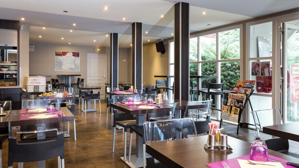 Un restaurante moderno con varias mesas y sillas, un ventanal con vistas a zonas verdes y un mapa en la pared.