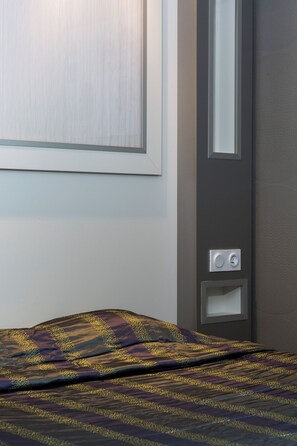 A hotel room with a bed, a wall-mounted light switch, and a door. - Initial By Balladins Lyon-chanas (Chanas)