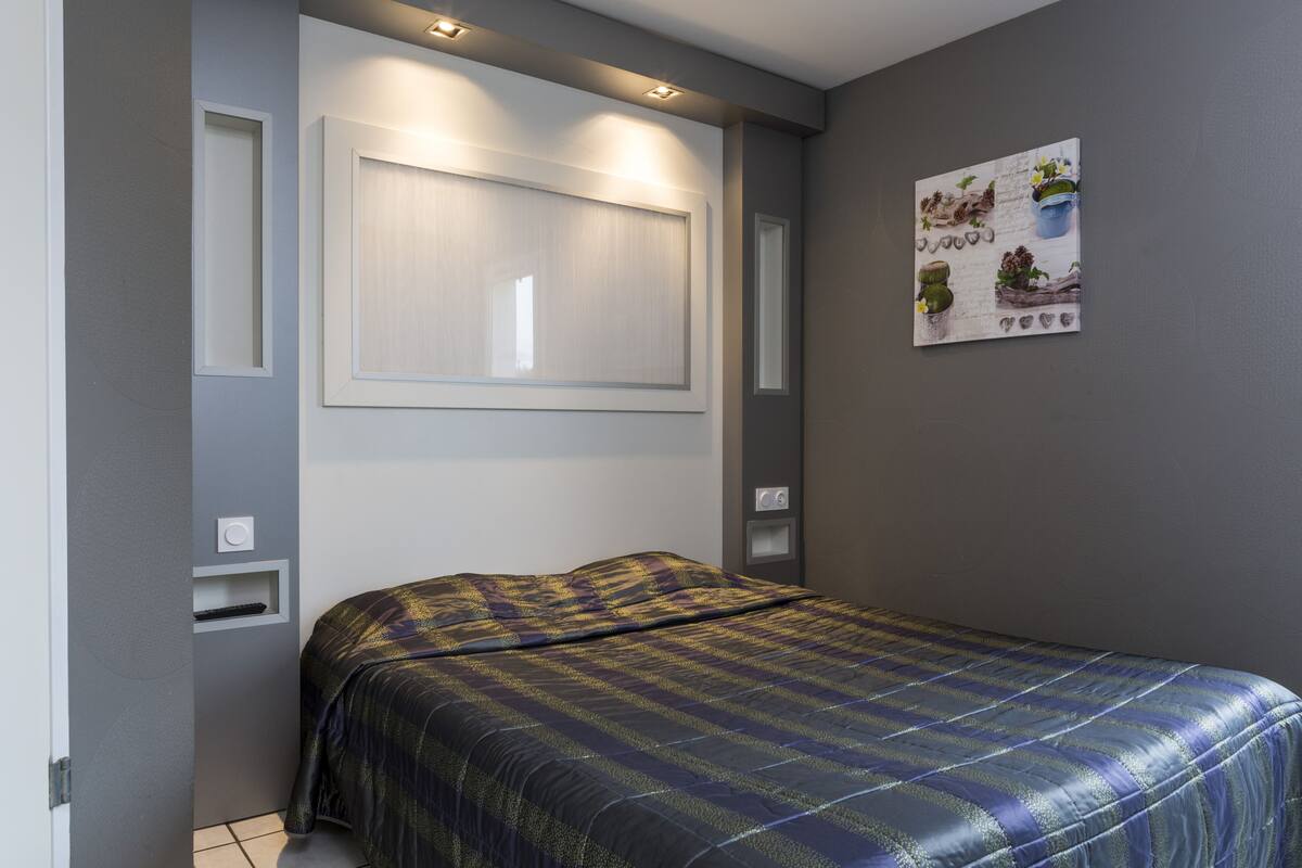 A bedroom with a bed, a window, a wall-mounted artwork, and built-in lighting.