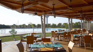 An outdoor restaurant with tables and chairs, a pool in the background, and ceiling fans. - The Grand Bhagwati Seasons Rajkot (Rajkot)