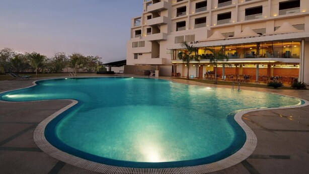A modern hotel with a large swimming pool, outdoor seating, and a restaurant area. - The Grand Bhagwati Seasons Rajkot (Rajkot)