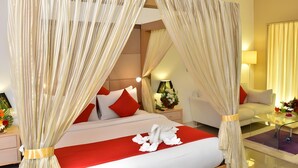 A hotel room with a bed, red and white bedding, a nightstand with a lamp, and a chair. - The Grand Bhagwati Seasons Rajkot (Rajkot)