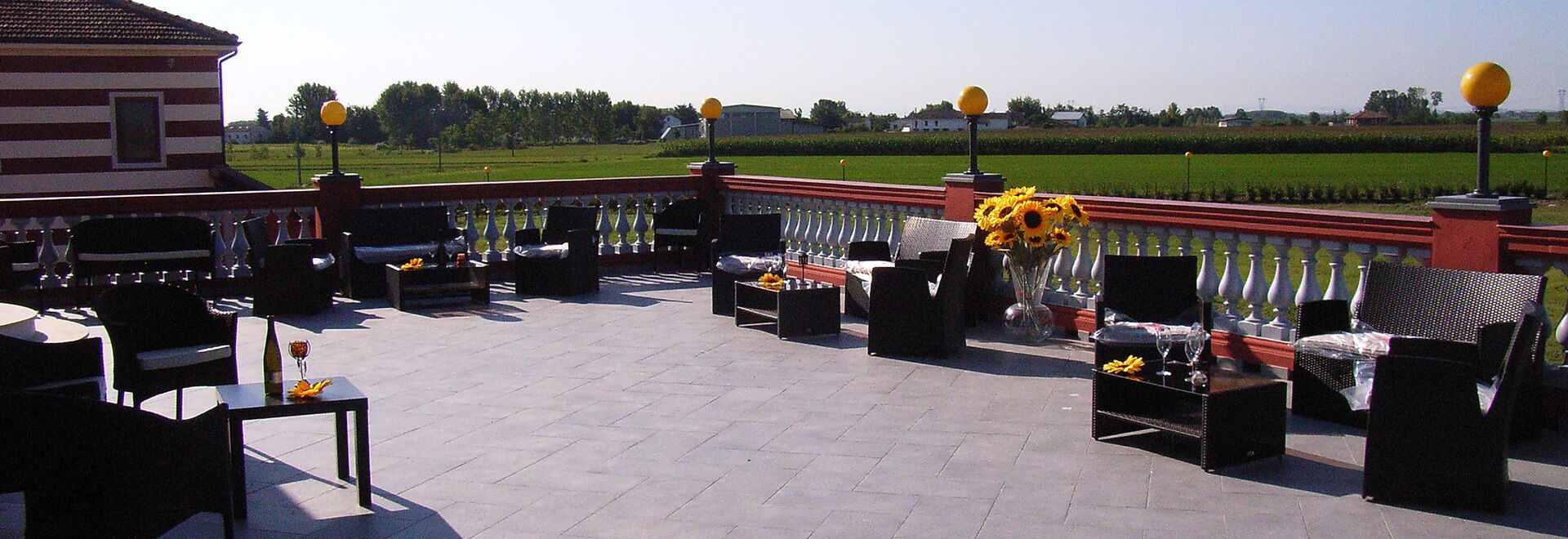 An outdoor patio with tables and chairs, a flower arrangement, and a view of a green field.