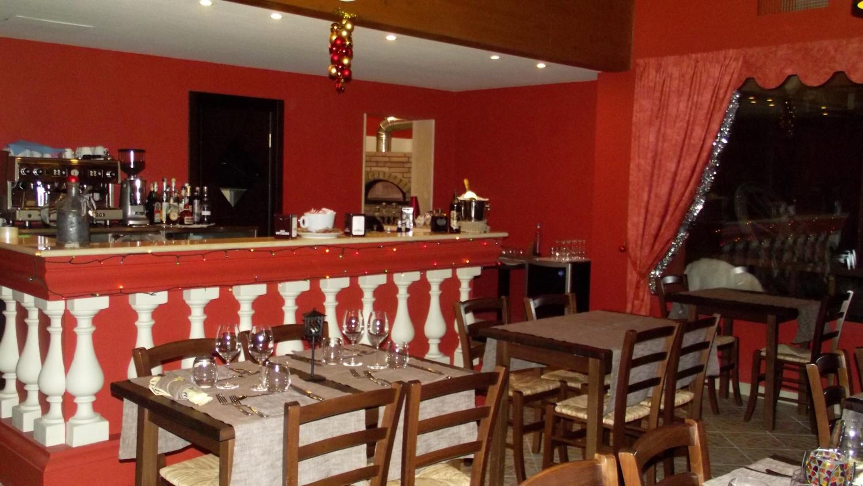 A restaurant with a red interior, a bar area with various bottles, and tables set for dining.