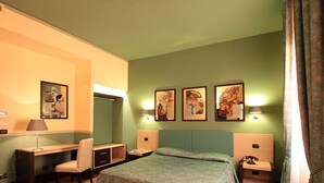 Una habitación de hotel con una cama, un escritorio, una silla y tres lámparas fijadas a la pared.