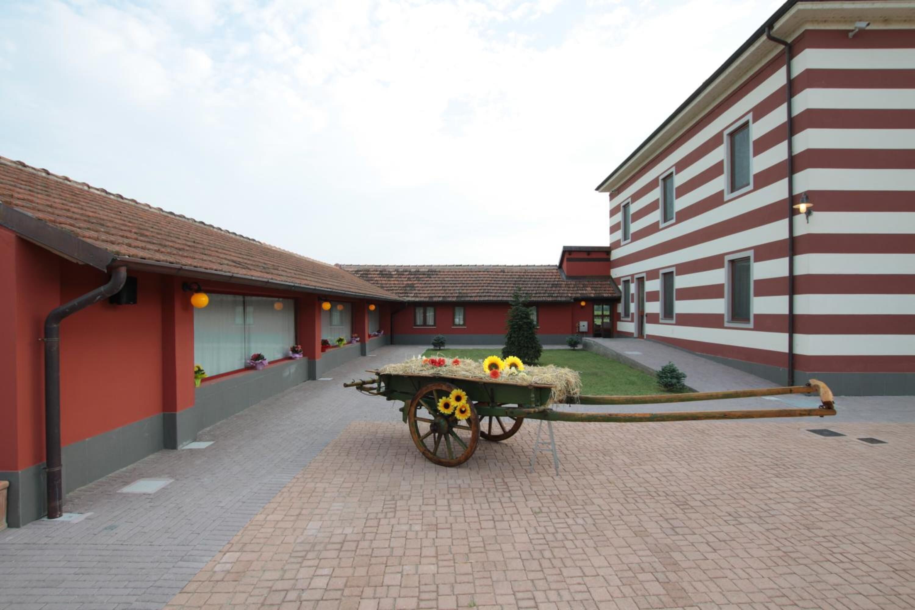 Un patio con un carruaje de madera tradicional lleno de heno y flores, rodeado de edificios con franjas rojas y blancas.