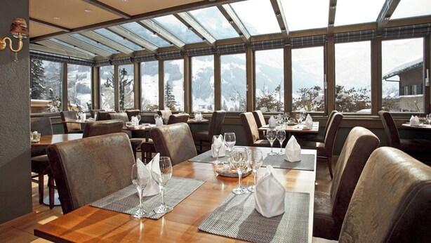 A restaurant with tables set for dining, large windows, and a view of mountains. - Steinmattli Hotel (Adelboden)