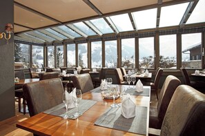 Un restaurante con mesas dispuestas para comer, ventanas amplias y vistas a montañas.