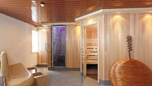A modern spa room with a glass door leading to a steam room, a wooden cabinet, and a unique spherical sculpture. - Steinmattli Hotel (Adelboden)
