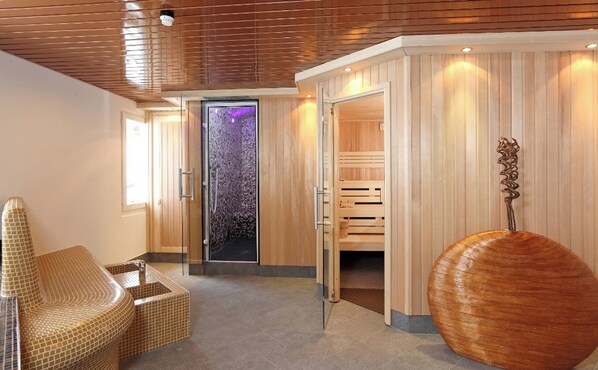 A modern spa room with a glass door leading to a steam room, a wooden cabinet, and a unique spherical sculpture.