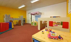 A playroom with a wooden table, play structures, and storage units.