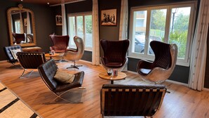A room with a wooden ceiling, large windows, a mirror, and modern chairs. - Steinmattli Hotel (Adelboden)