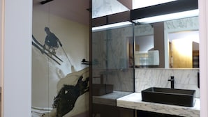 A bathroom with a glass shower enclosure, a marble sink, and a large mirror.