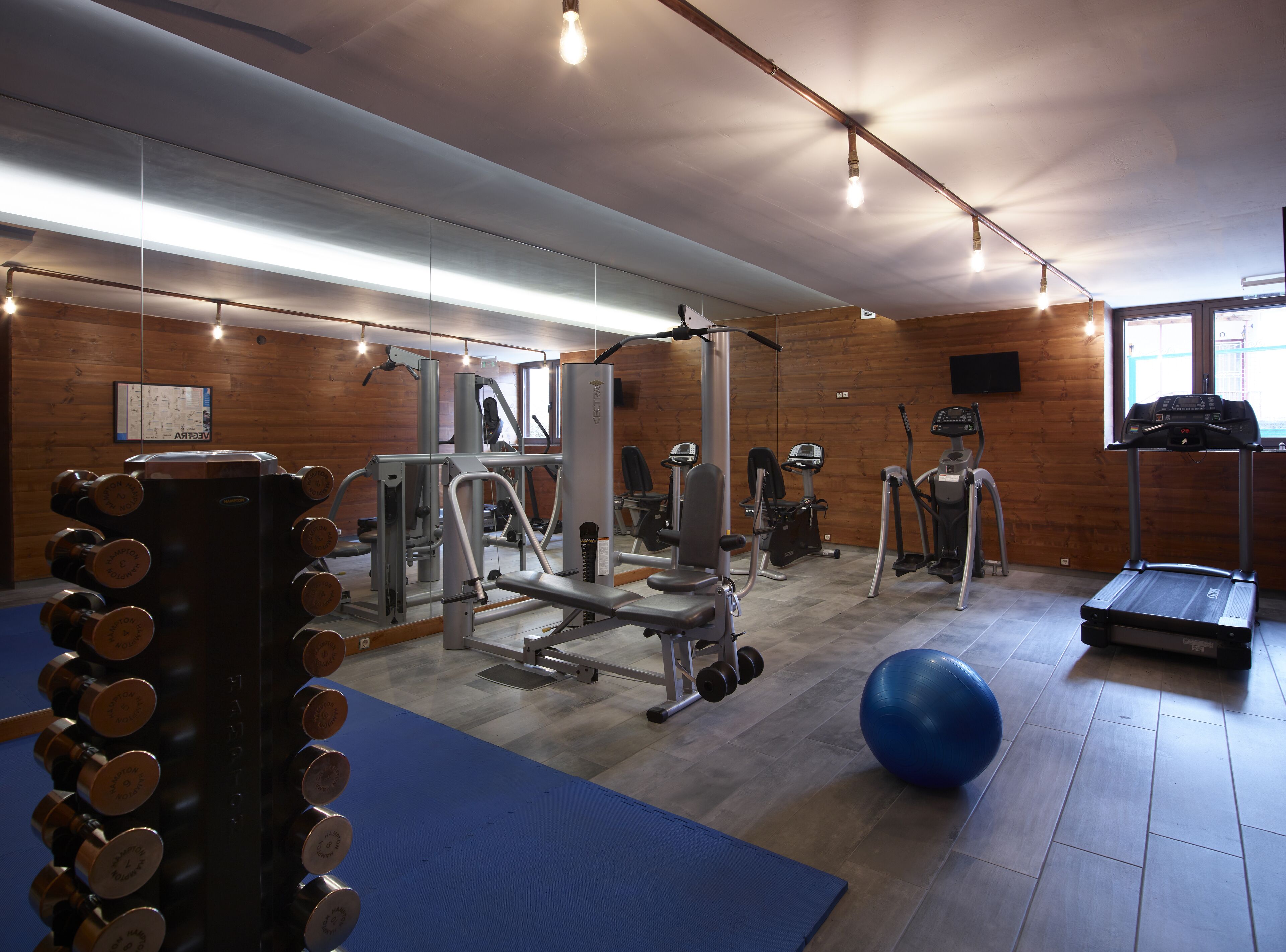 A gym with various exercise equipment, including dumbbells, a bench press, and cardio machines.