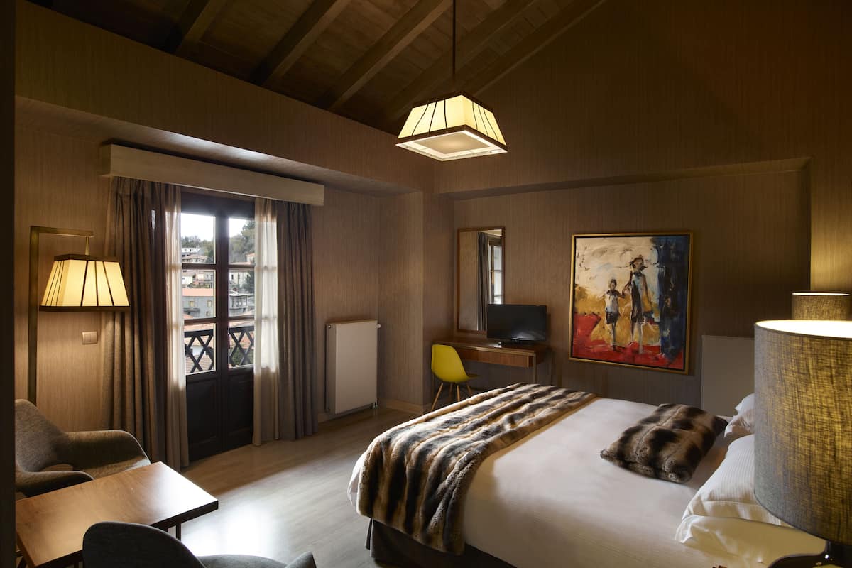 A hotel room with a bed, a desk, a chair, a TV, and a painting on the wall.