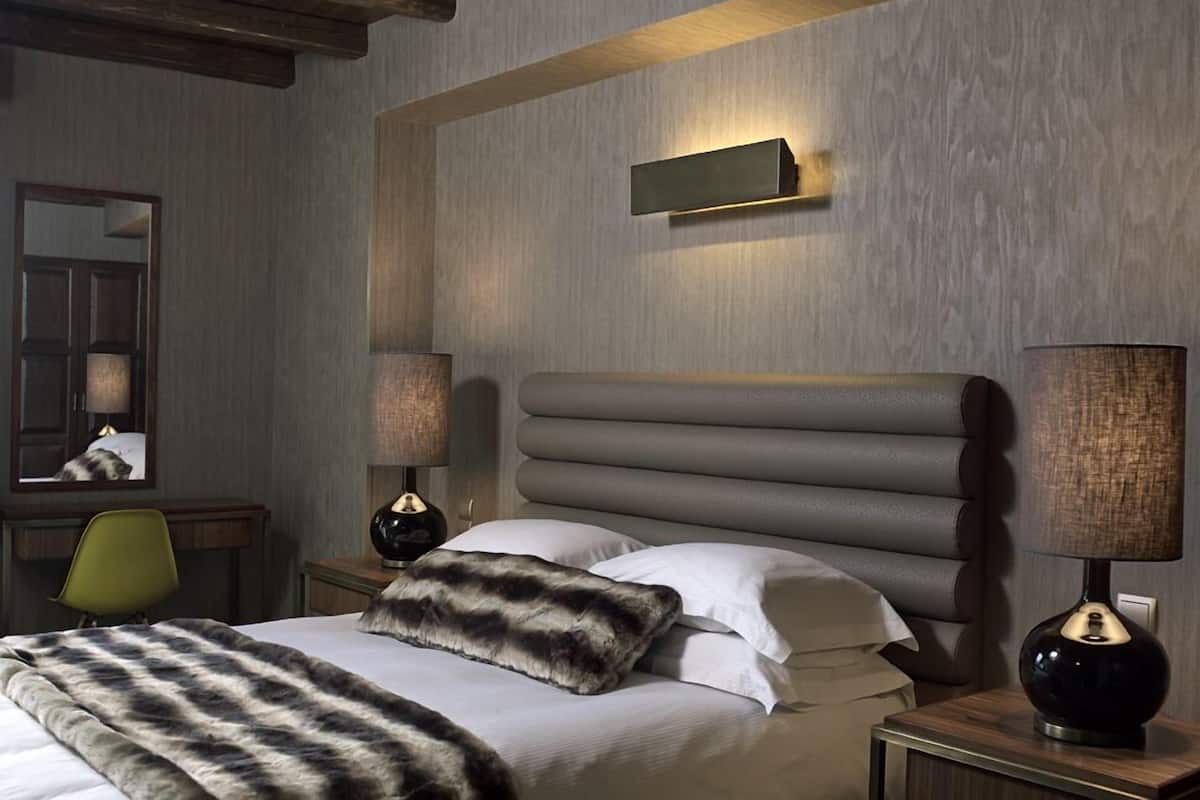 A modern hotel room with a large bed, two bedside tables with lamps, a mirror, and a wooden ceiling.