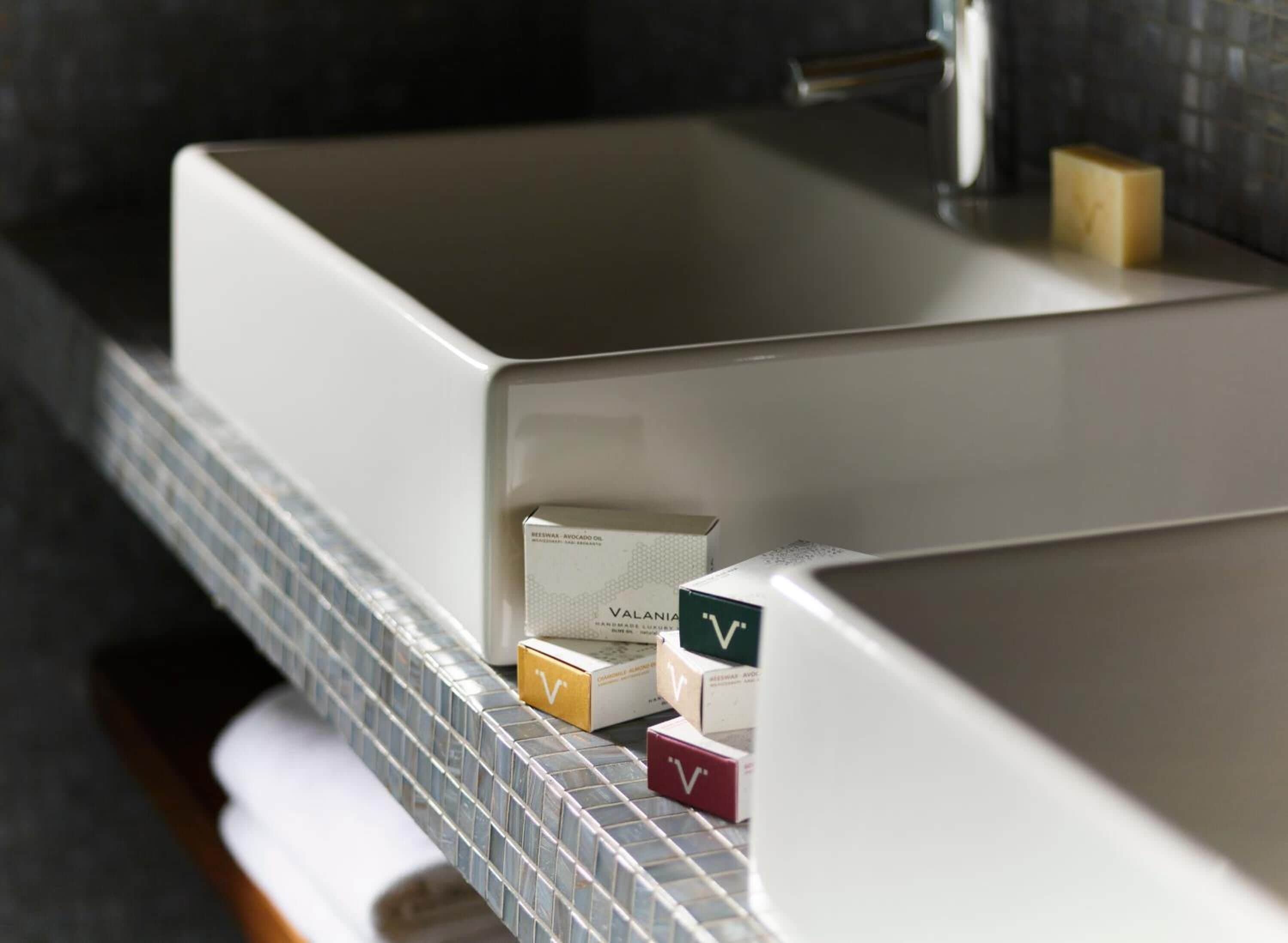 A bathroom with a white sink, a tiled backsplash, and three boxes labeled 'Valania' on the countertop.