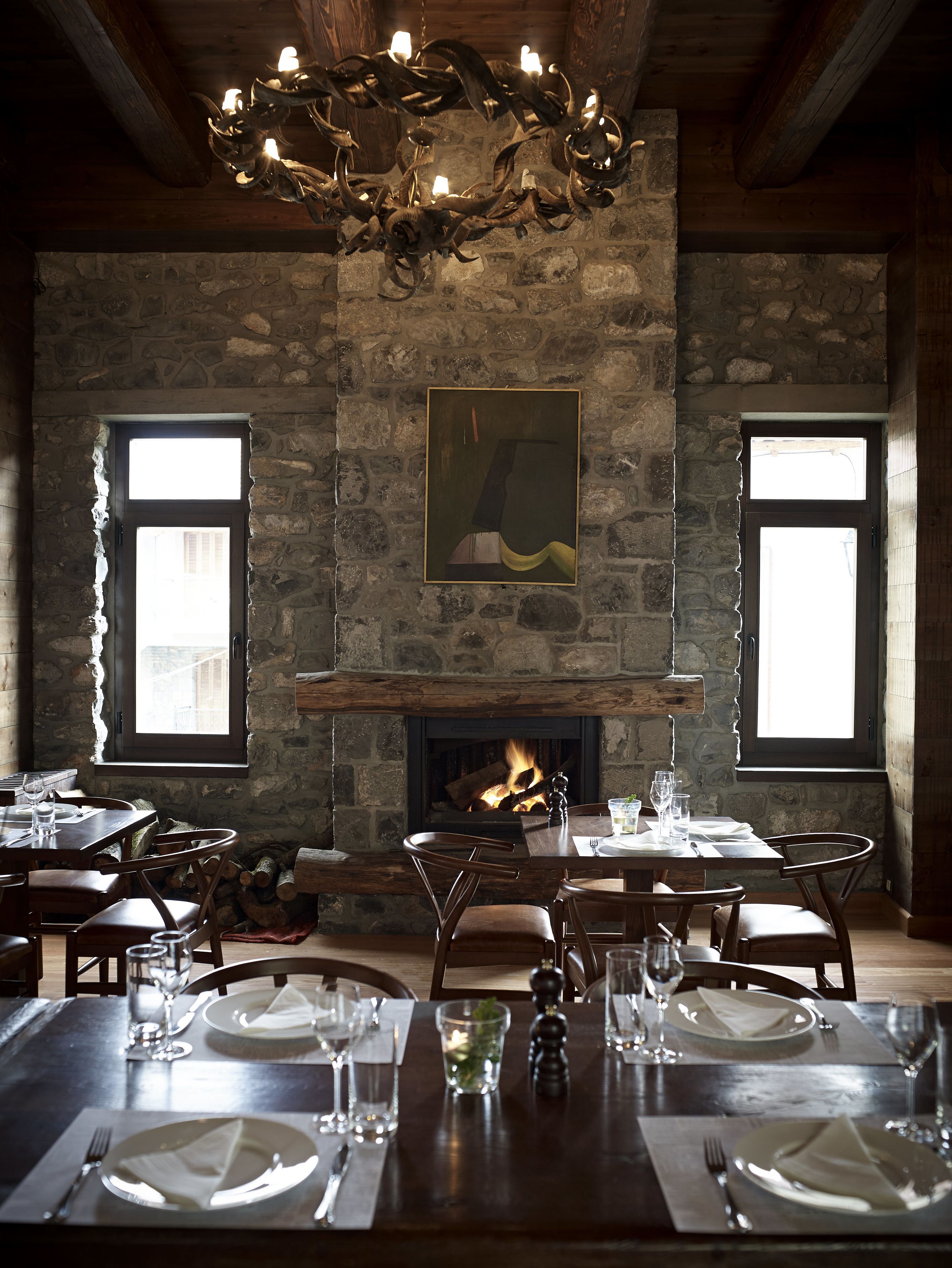 Une salle à manger aux murs en pierre, dotée d’une cheminée et d’un lustre. Les tables sont dressées avec des assiettes, des verres et des couverts.