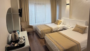 Une chambre d’hôtel avec deux lits, un bureau doté d’une bouilloire et de tasses, une chaise et une grande fenêtre avec des rideaux.
