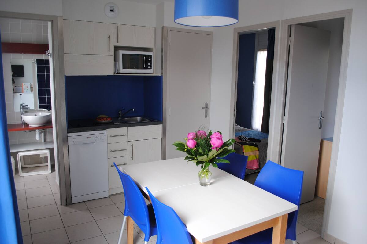 Cocina compacta con microondas, lavamanos y comedor con mesa y sillas.