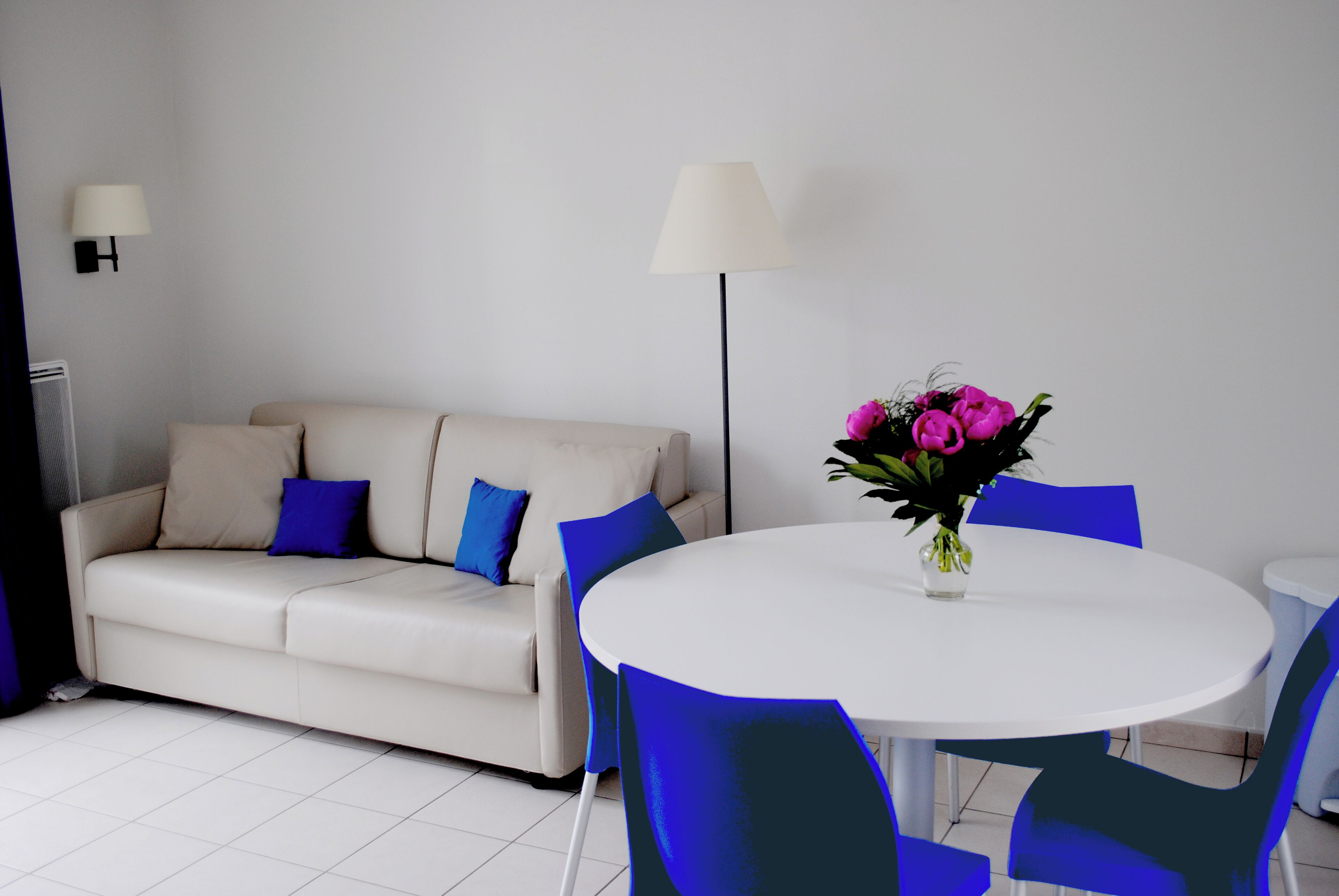 A modern living room with a white sofa, blue cushions, a round white table, and blue chairs.