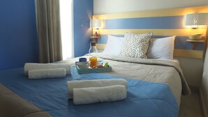 Habitación de hotel con una cama bien hecha, una mesita de noche con lámpara, un jarrón y una bandeja con alimentos para el desayuno.