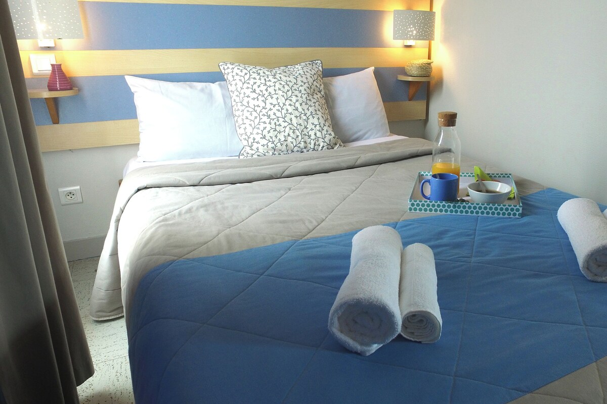Ein Hotelzimmer mit Bett, Kissen, einem Nachttisch mit Lampe, einer Flasche, einer Schale und gerollten Handtüchern.
