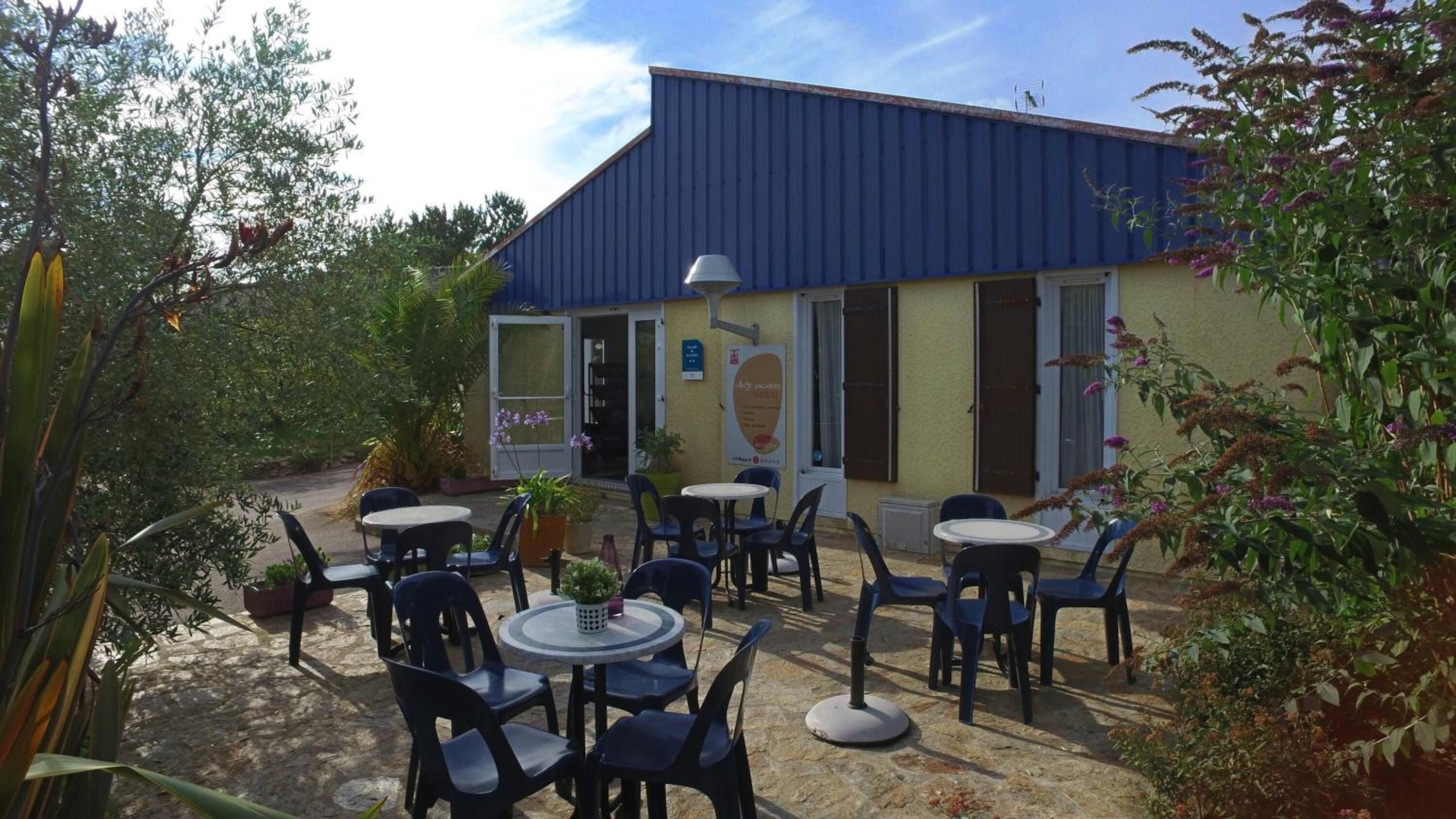 Een terras met tafels en stoelen voor een gebouw met een blauw dak.