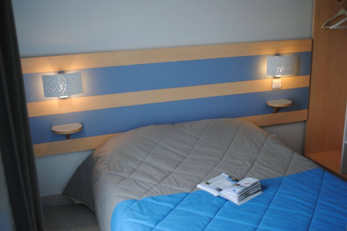 Habitación de hotel con cama, mesita de noche e iluminación en la pared.