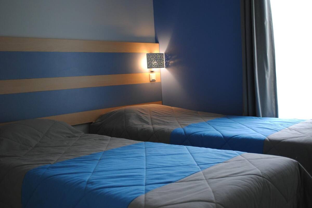 Habitación de hotel con dos camas, una luz nocturna en la pared y una ventana con cortinas.