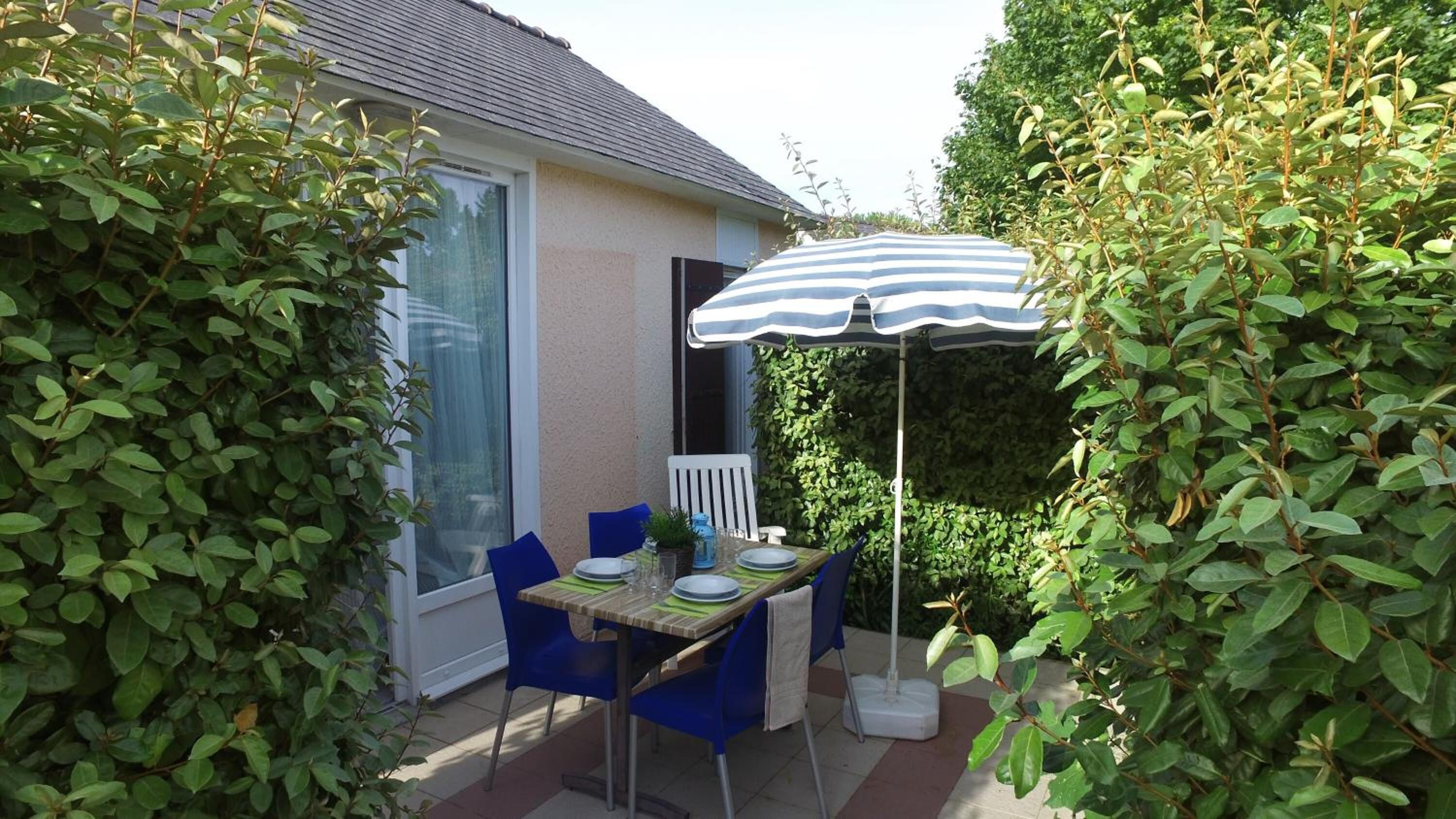 A patio with a table and chairs, a striped umbrella, and a house in the background.