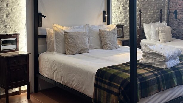 A four-poster bed with white linens and pillows, a dark wooden frame, a nightstand with a small table, and a patterned rug on the floor. - Estancia Los Platanos (Valentines)