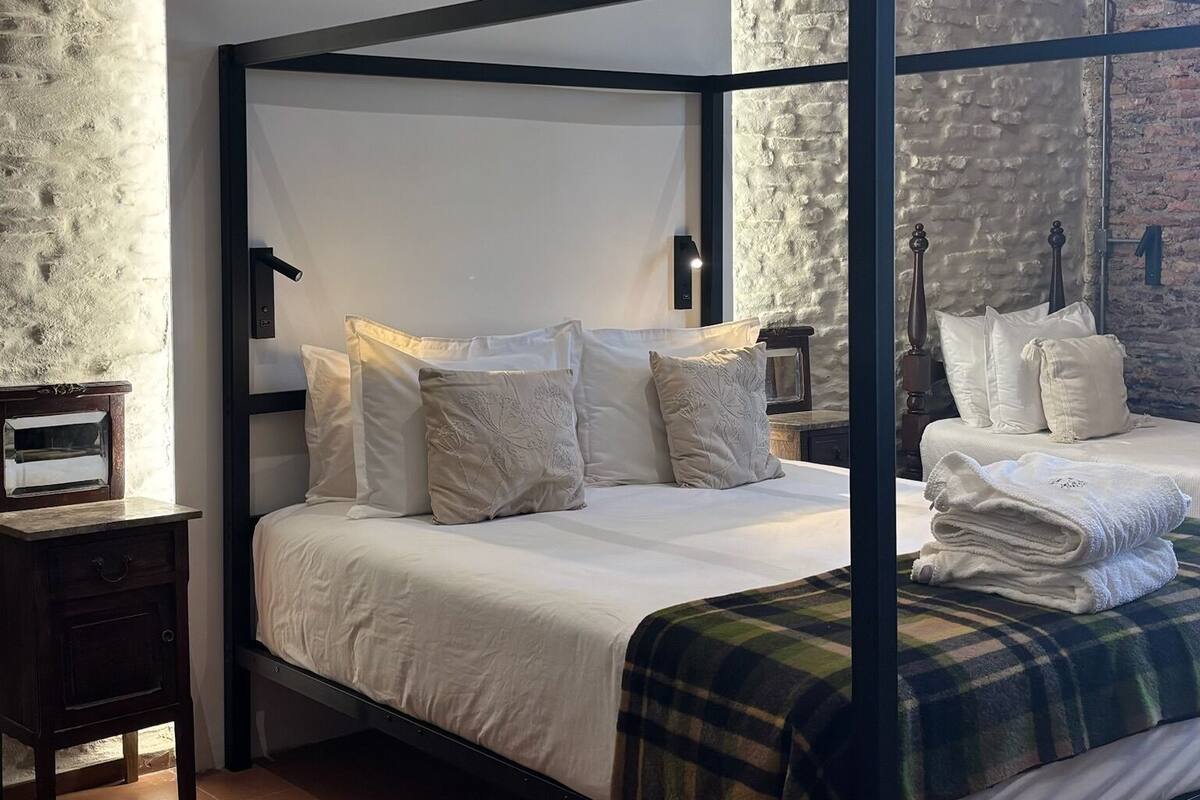 A four-poster bed with white linens and pillows, a dark wooden frame, a nightstand with a small table, and a patterned rug on the floor.