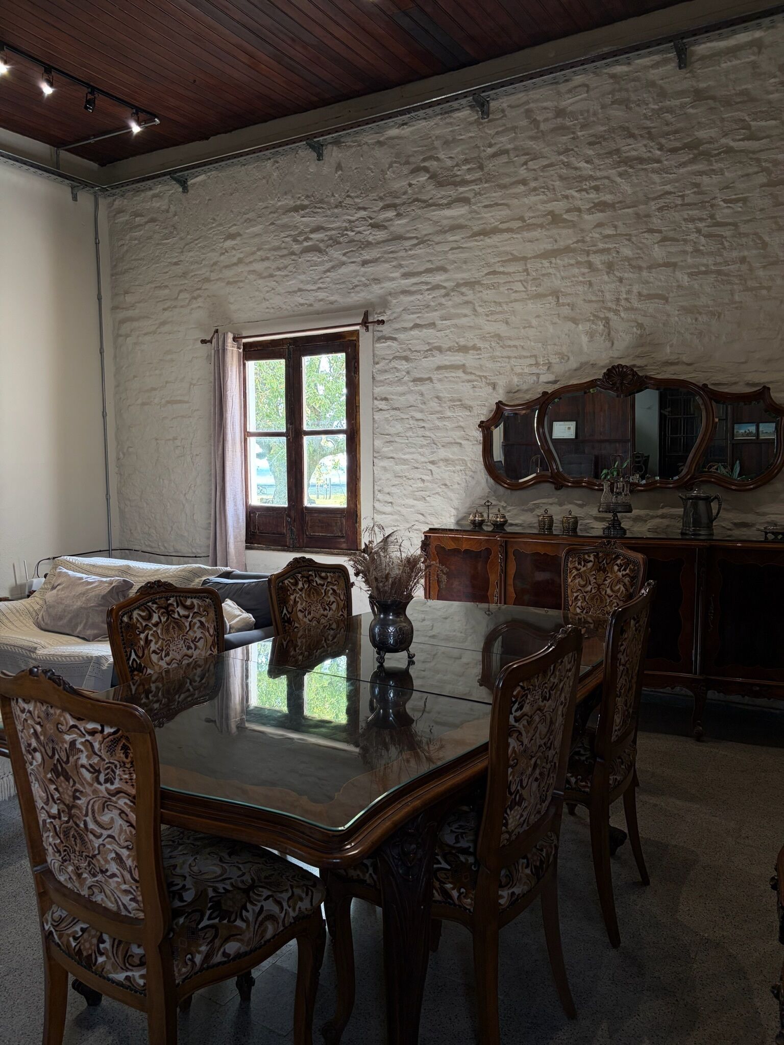 A dining area with a wooden table and chairs, a stone wall, and a window with curtains.