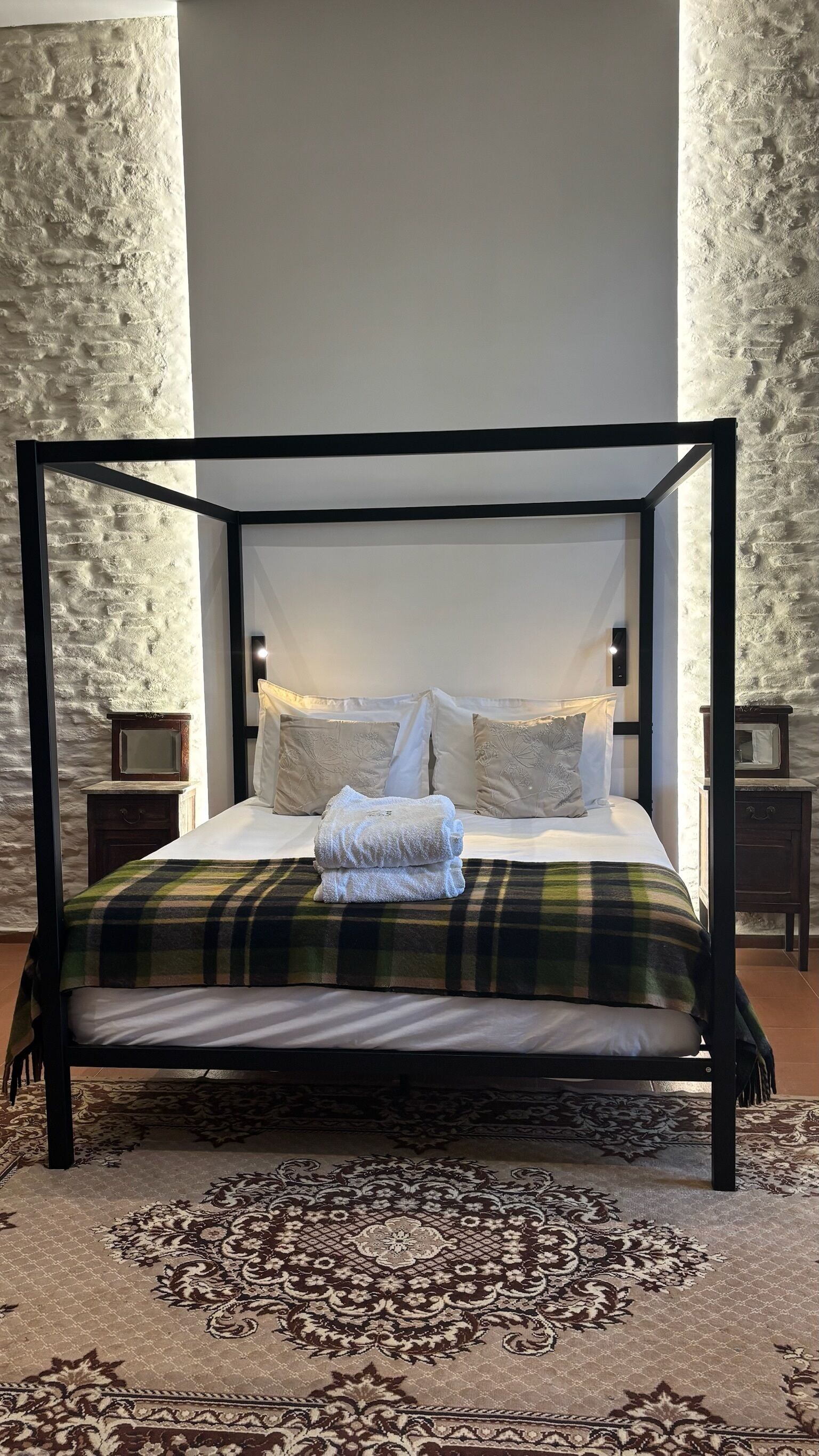 Una cama con dosel con una colcha escocesa, almohadas blancas y una toalla doblada.