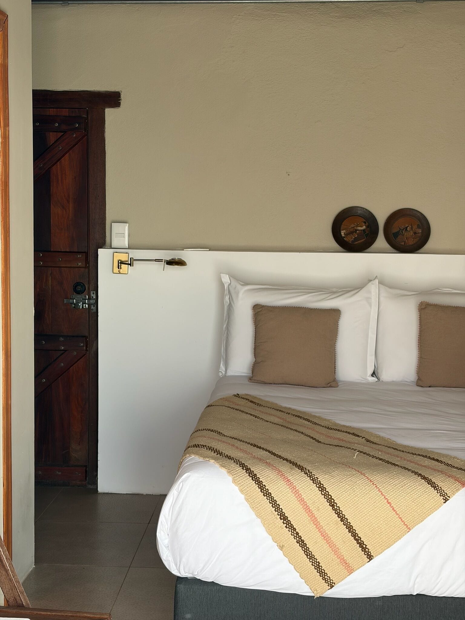 Un dormitorio con una cama, almohadas, una manta, una puerta y relojes en la pared.