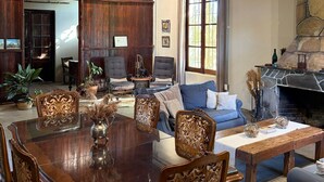 A spacious living room with a wooden ceiling, a stone fireplace, and a dining area with a large wooden table and ornate chairs. - Estancia Los Platanos (Valentines)