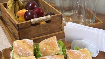 A wooden tray with sandwiches, a fruit basket, and clear glasses.