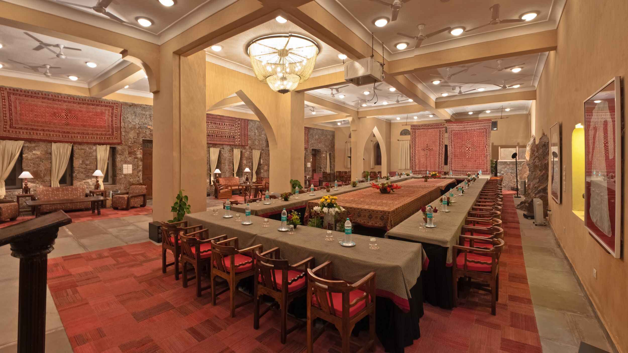 Une salle de banquet spacieuse, dotée de hauts plafonds, de lustres et d’une longue table à manger dressée pour un événement formel.