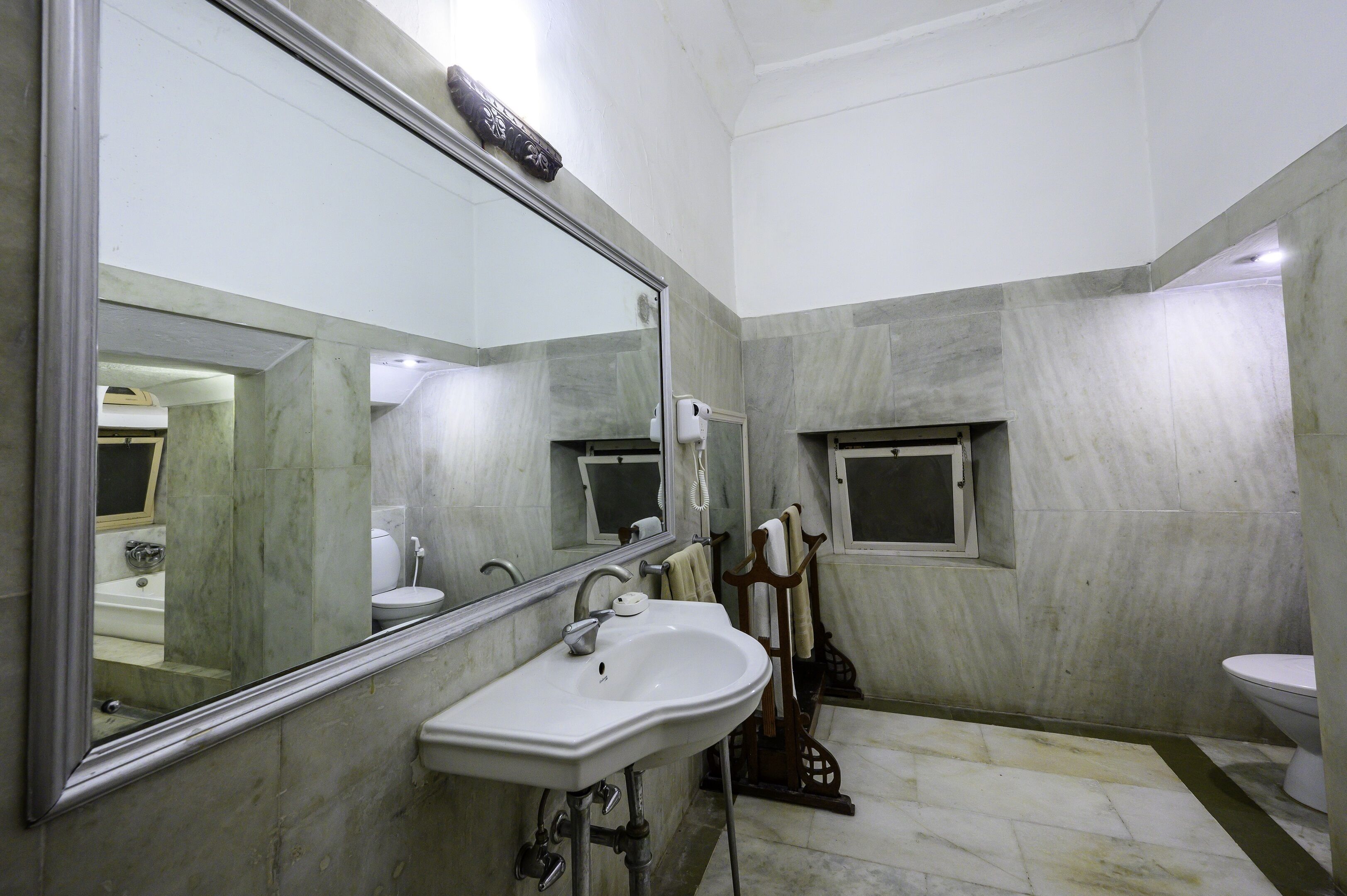 A bathroom with a large mirror, a sink, a toilet, and a window.