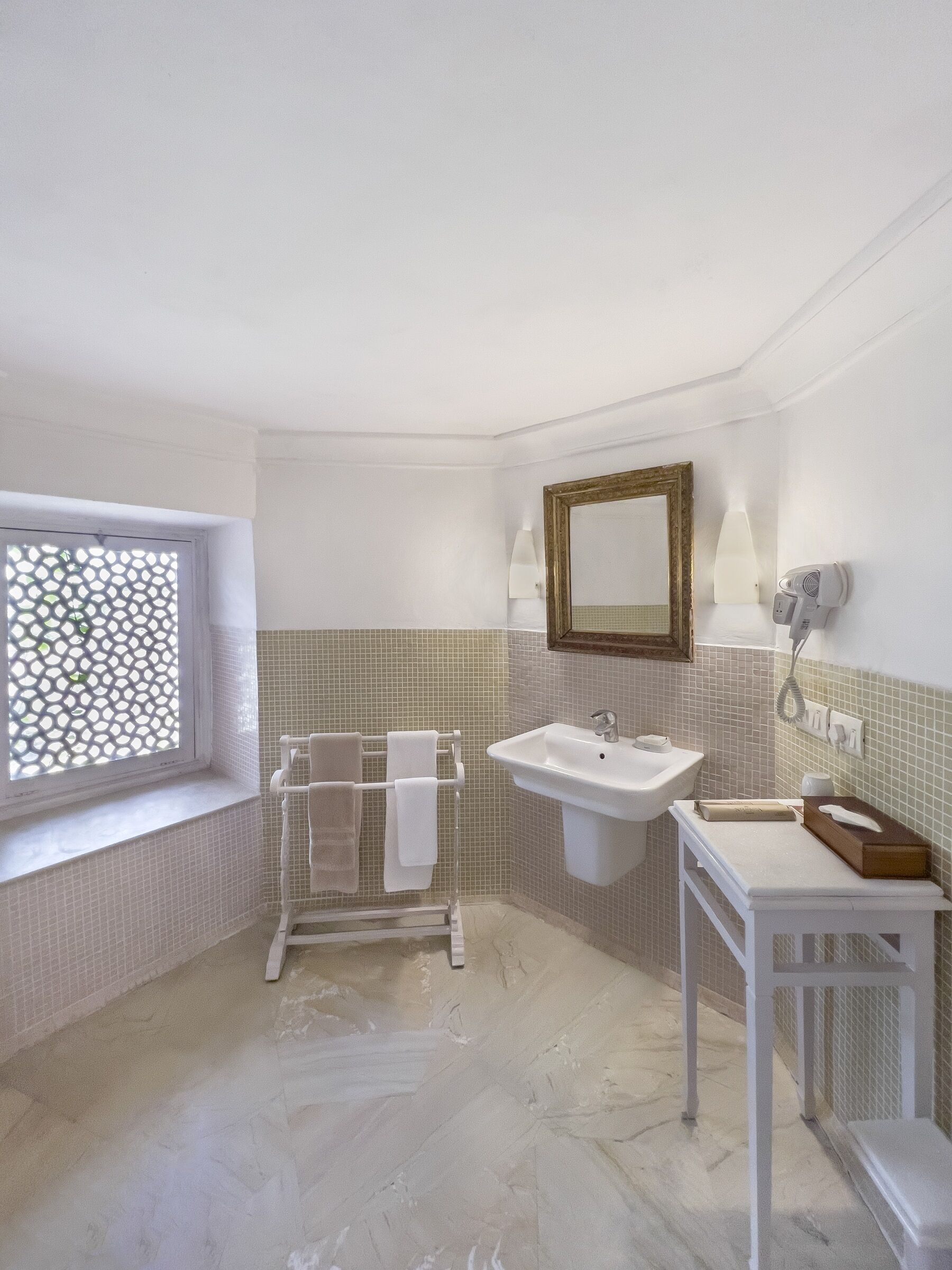 Une salle de bain équipée d’un lavabo, d’un miroir, d’un porte-serviettes et d’une fenêtre ornée d’un motif en treillis.