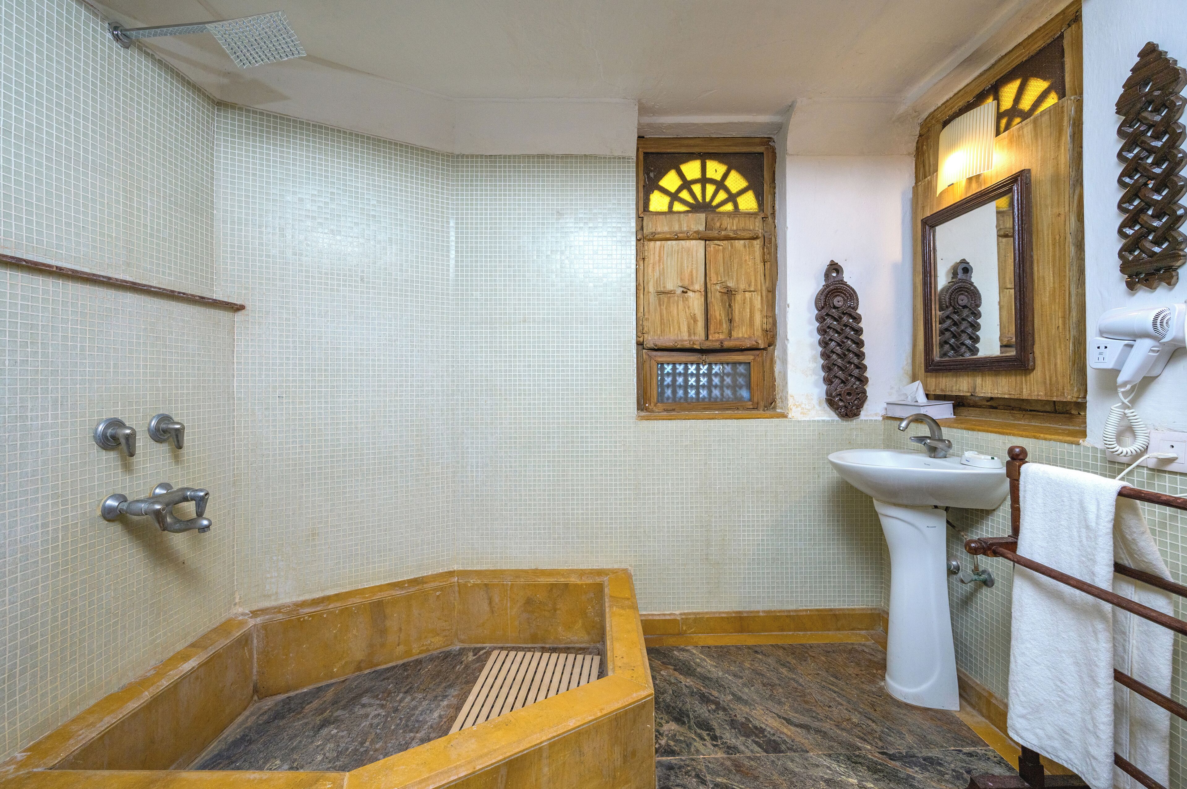 Un baño con bañera, lavamanos, espejo y ventana con diseño decorativo.