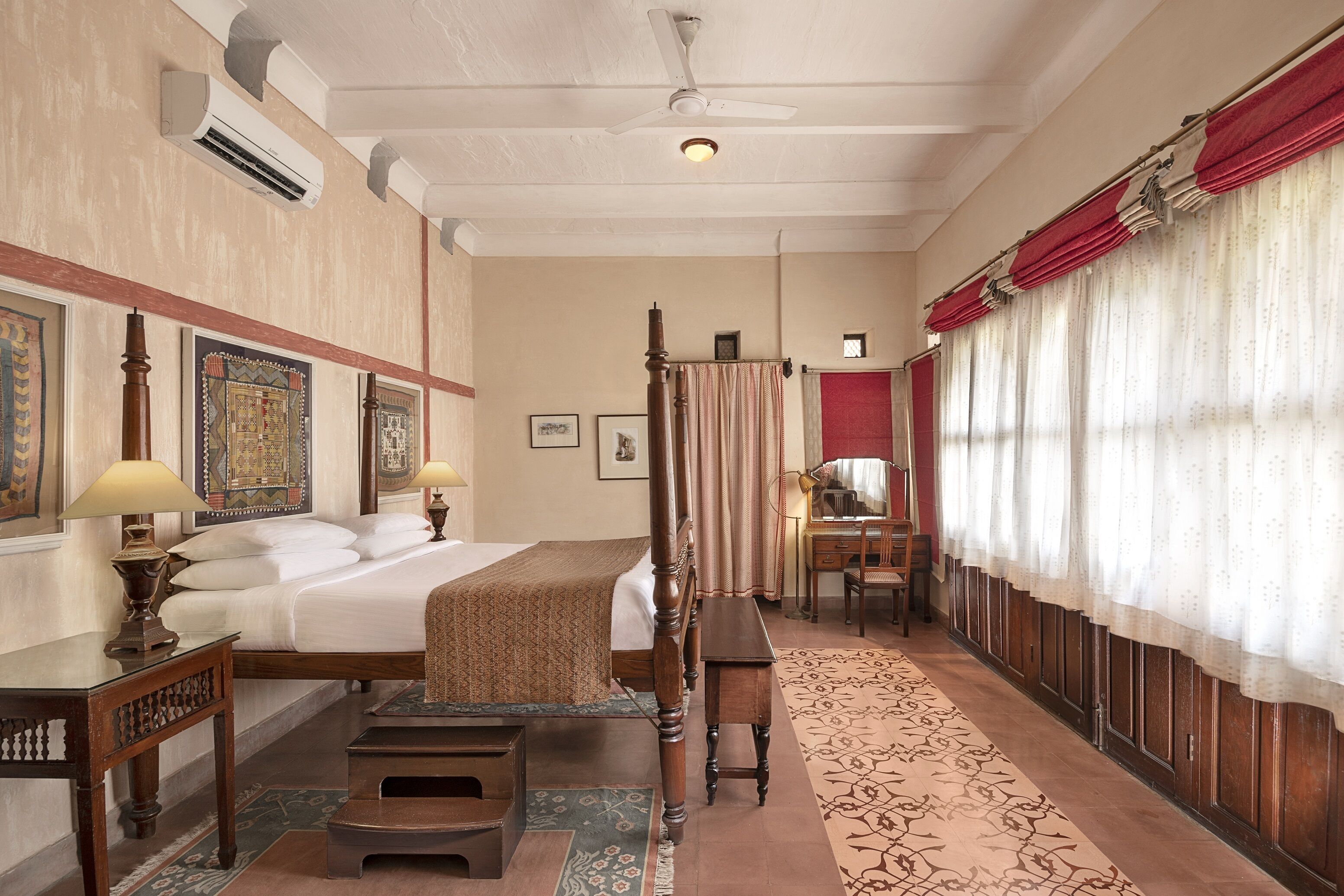 A hotel room with a large bed, a desk, a chair, a wardrobe, and a mirror.