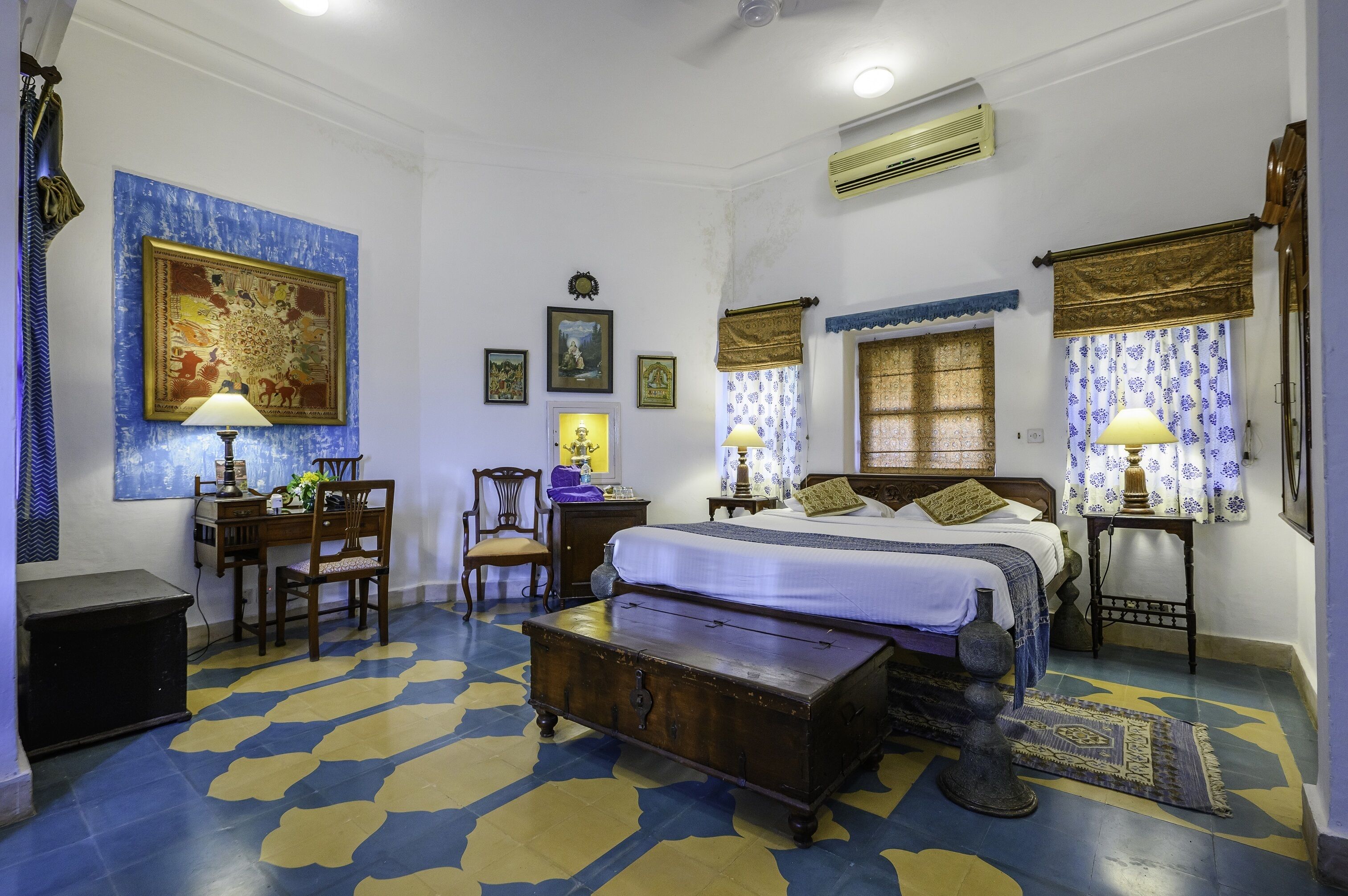 Une chambre à coucher comprenant un lit, des tables de chevet, un bureau, des chaises, une commode et un grand tableau accroché au mur.