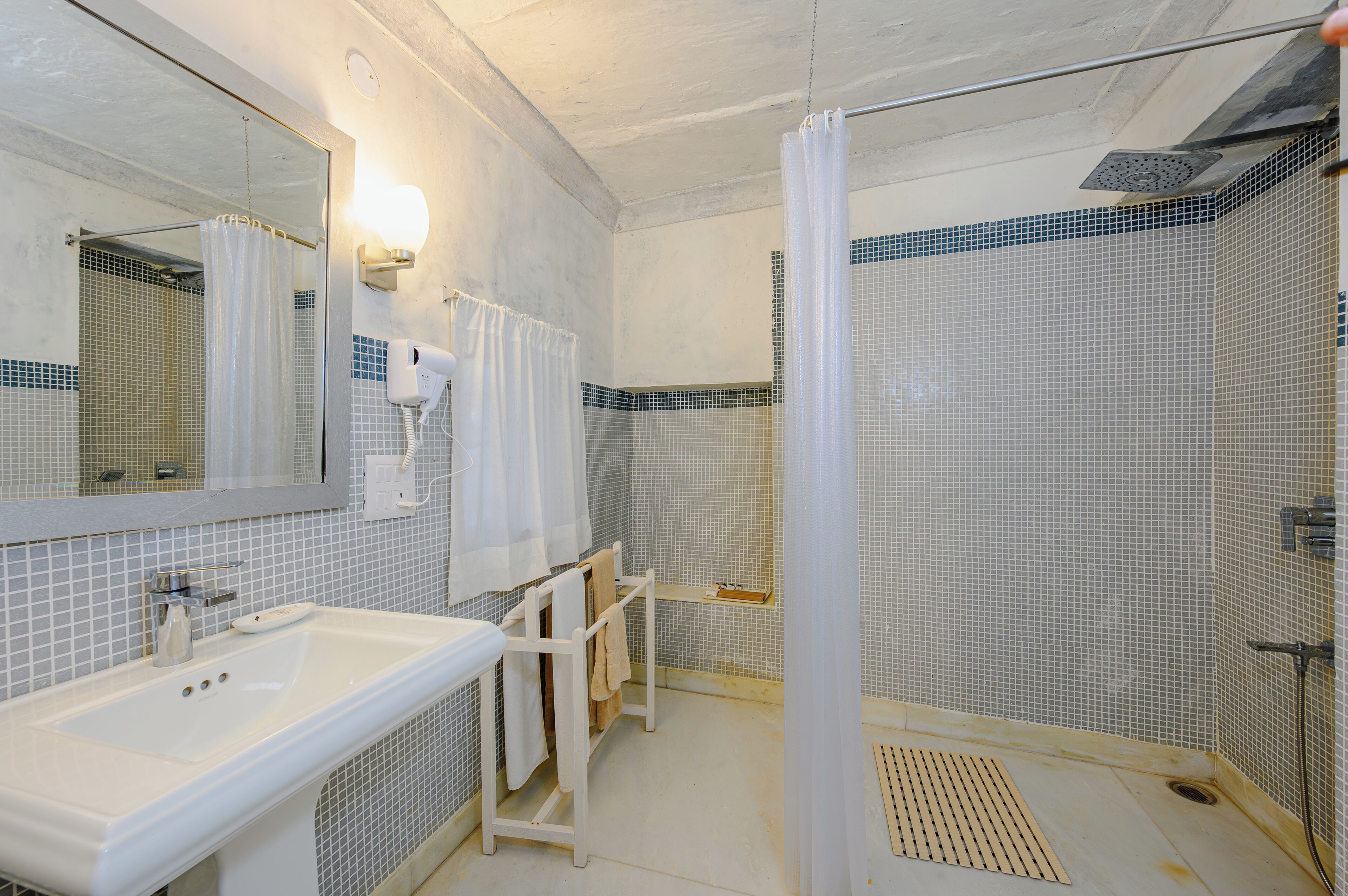 A bathroom with a white sink, a mirror, a shower with a glass door, and a tiled floor.