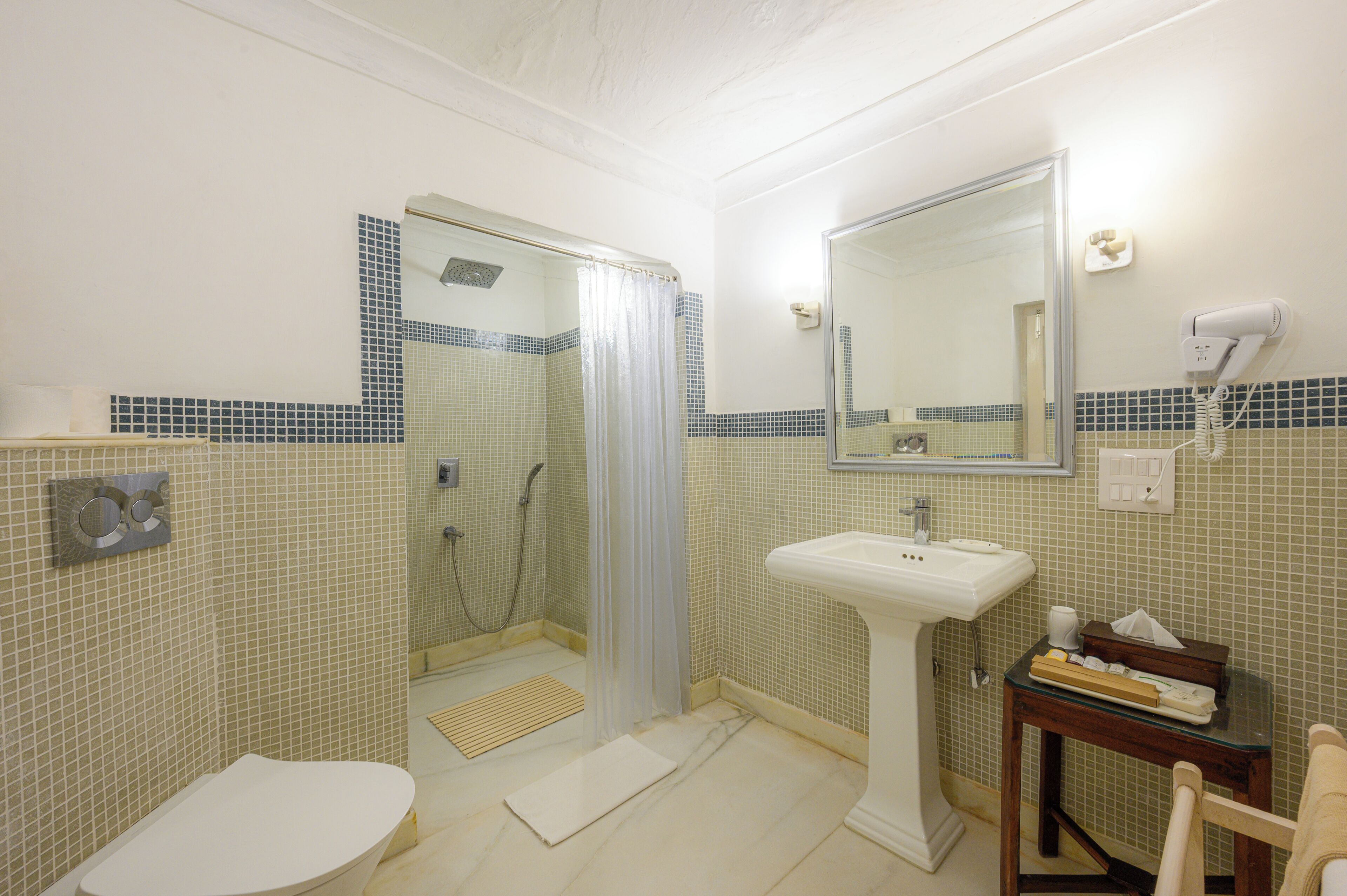A bathroom with a toilet, sink, shower, and a mirror.